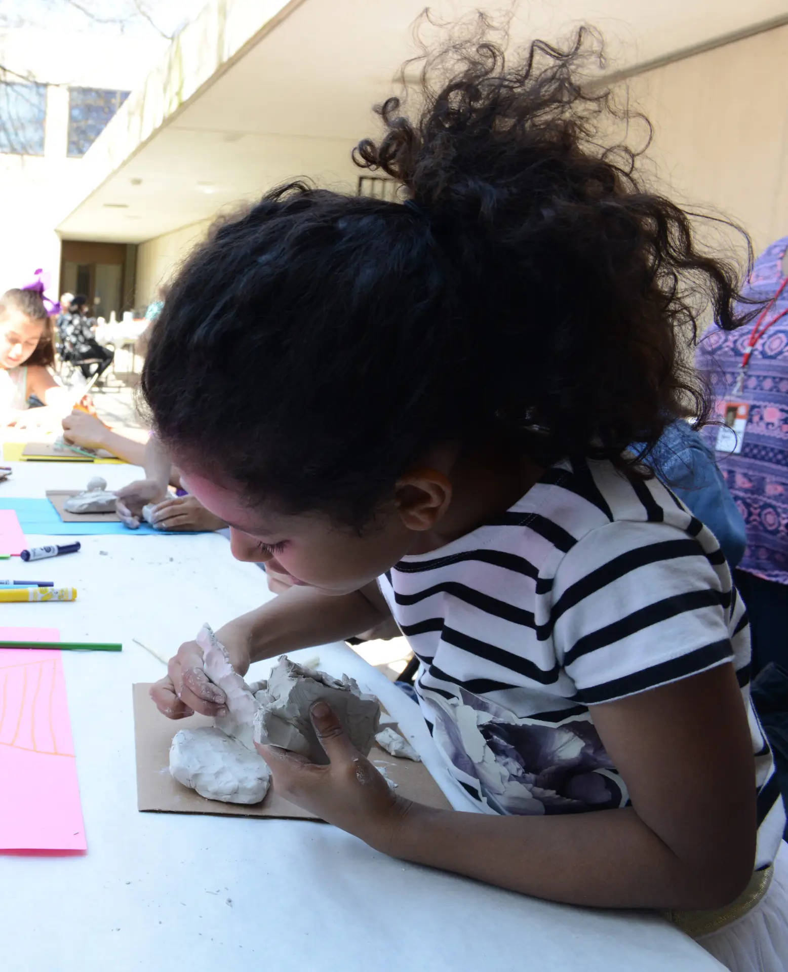 A child in a black and white striped shirt pinches lumps of clay together.