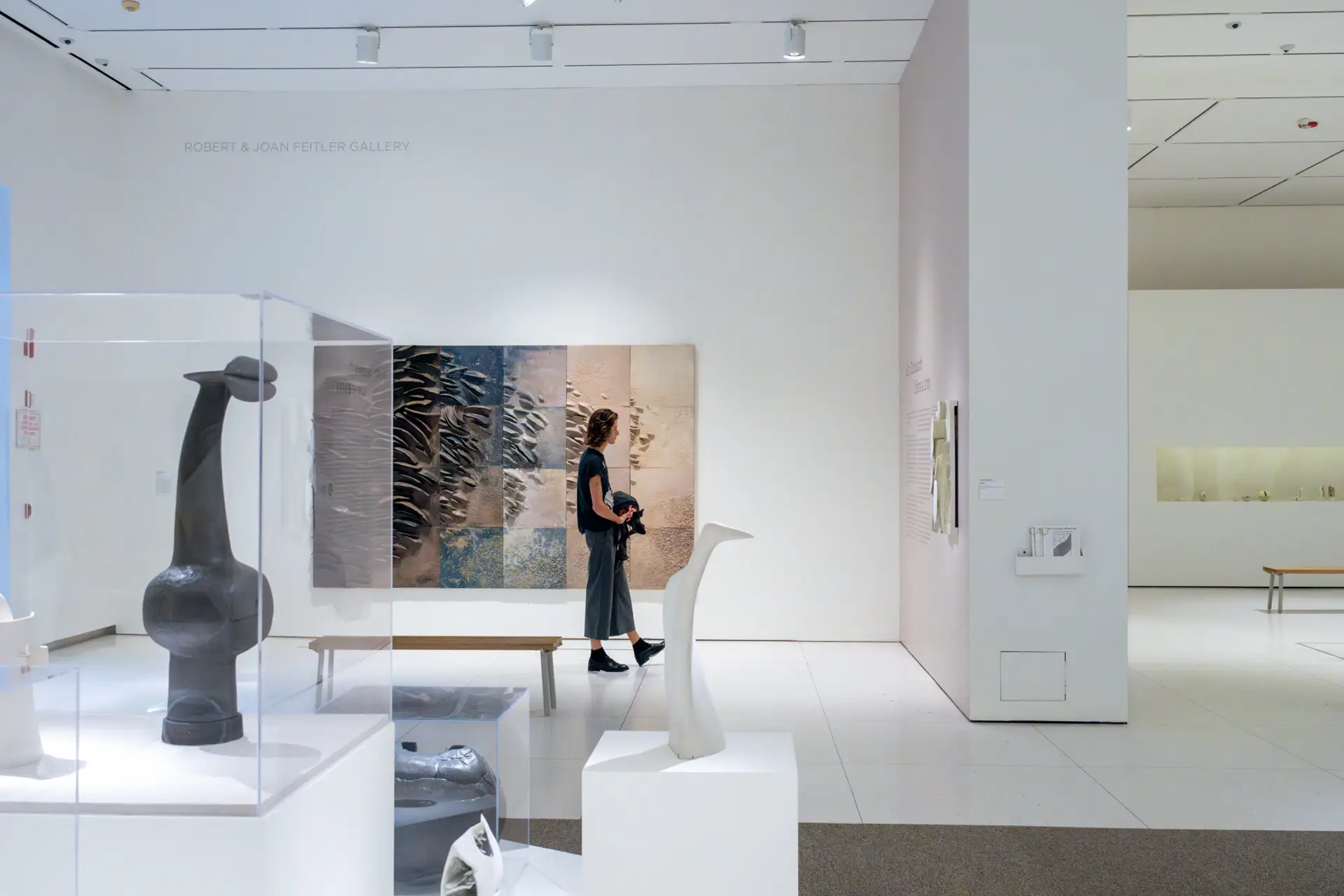 A person stands in front of a large, earth-toned clay tile mural reading explanatory text on the wall in a museum space.