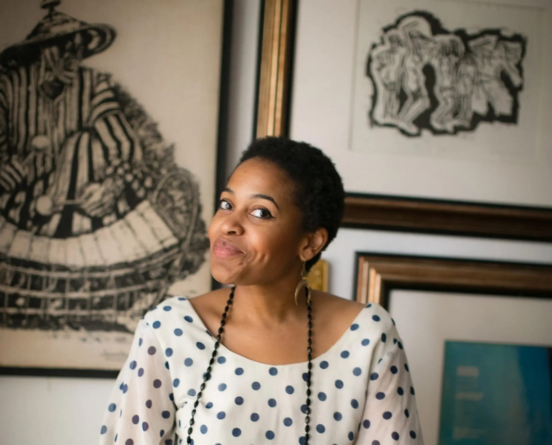 A portrait of Ayana Contreras wearing a white blouse with black polka dots and a long strand of black beads.