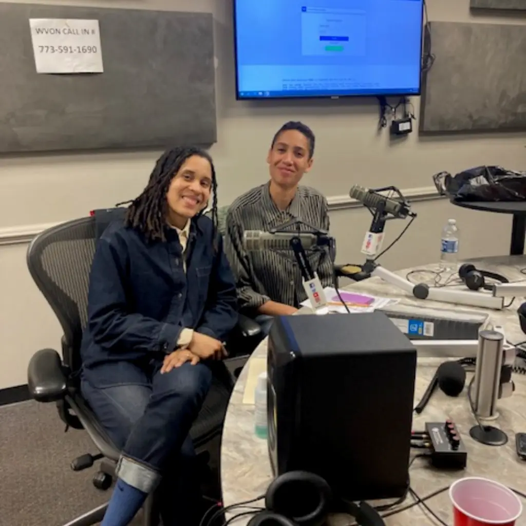 Ciera McKissick (left) and Dr. Pascal Ife Williams (right) are seated side by side at a round table with microphones in front of them and audio recording equipment scattered on the table.
