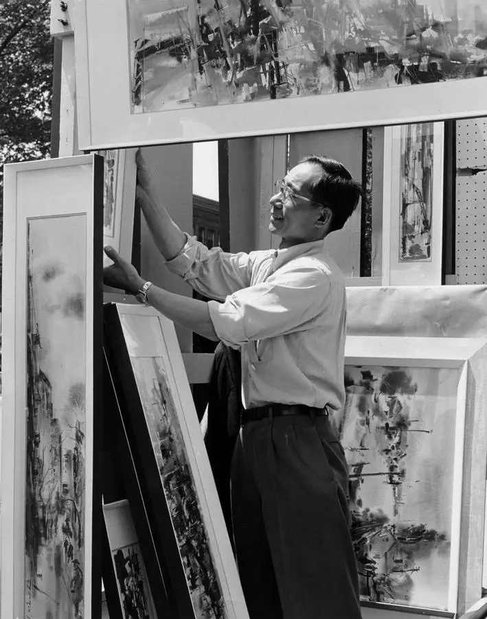 Vintage photo of a man standing in an art fair booth surrounded by paintings.